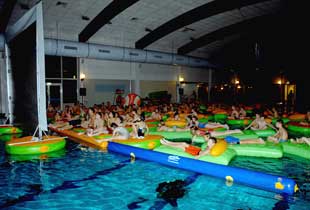 Menschen liegend auf Wassermatratzen im Hallenbad vor Kinoleinwand